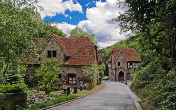 HD desktop wallpaper featuring charming stone houses in Kobern-Gondorf, Germany, surrounded by lush greenery and a clear blue sky.