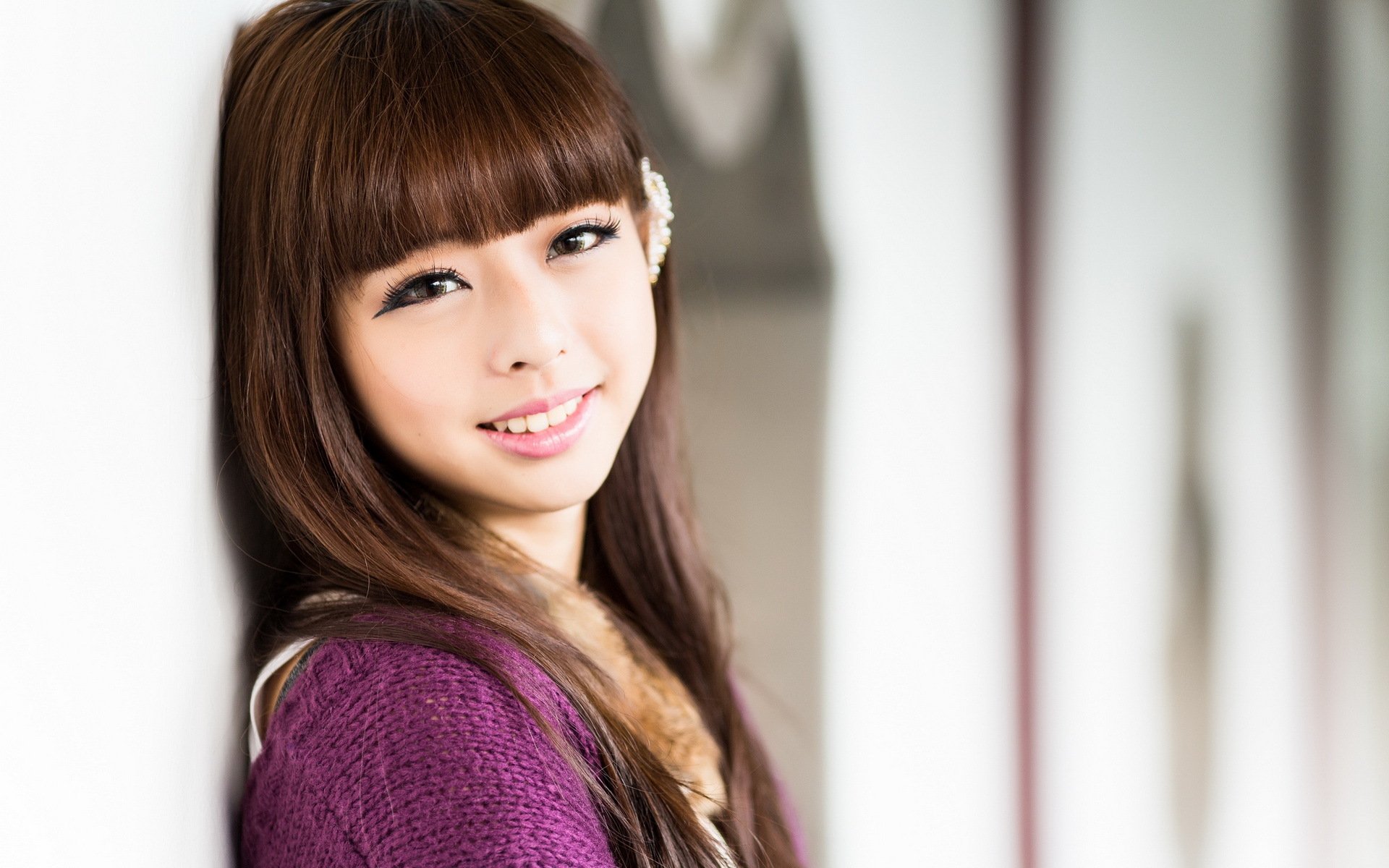 A smiling woman with long, straight brown hair leans against a wall, exuding warmth in this HD desktop wallpaper and background. Her cheerful expression brightens the scene.