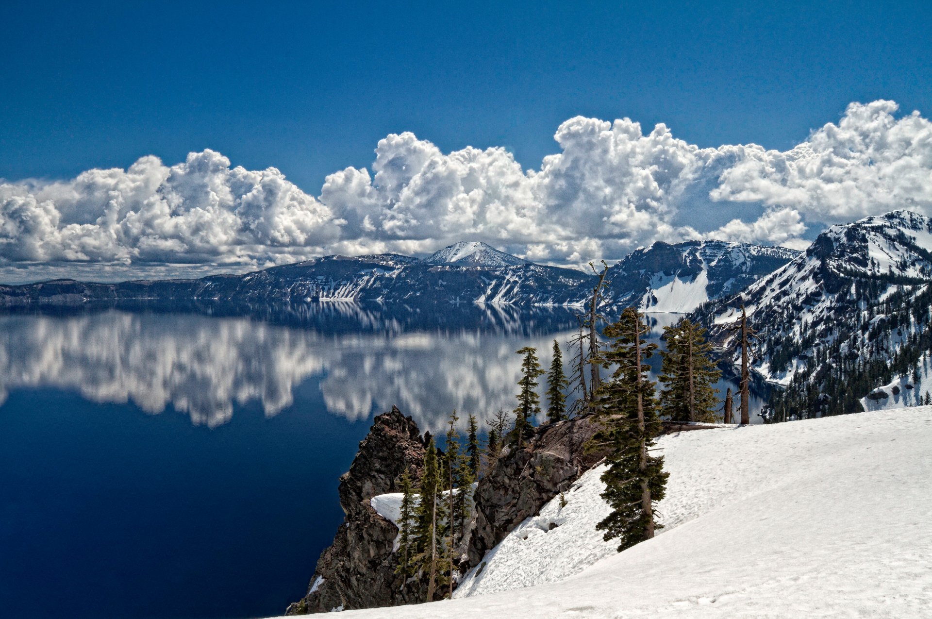 A stunning winter landscape featuring a serene lake reflecting towering clouds and majestic mountains, surrounded by snow-covered terrain, capturing the beauty of nature.