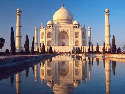 Stunning HD wallpaper of the Taj Mahal, showcasing its iconic white marble architecture and reflective pool, surrounded by lush greenery and clear blue skies.