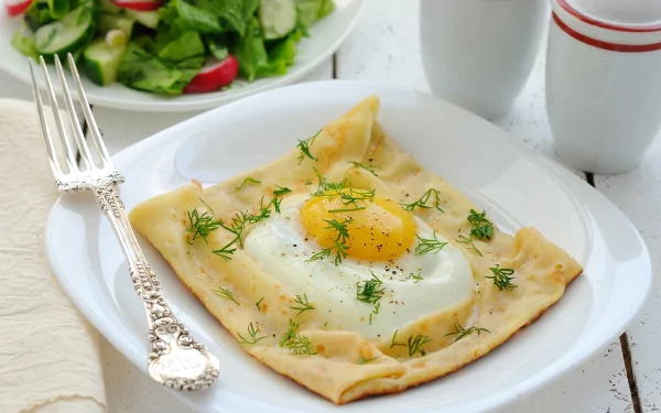 A beautifully presented plate of food features a perfectly cooked egg nestled in a delicate, golden crust, topped with fresh herbs, accompanied by a vibrant salad in the background.