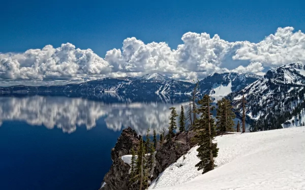 A stunning winter landscape featuring a serene lake reflecting towering clouds and majestic mountains, surrounded by snow-covered terrain, capturing the beauty of nature.