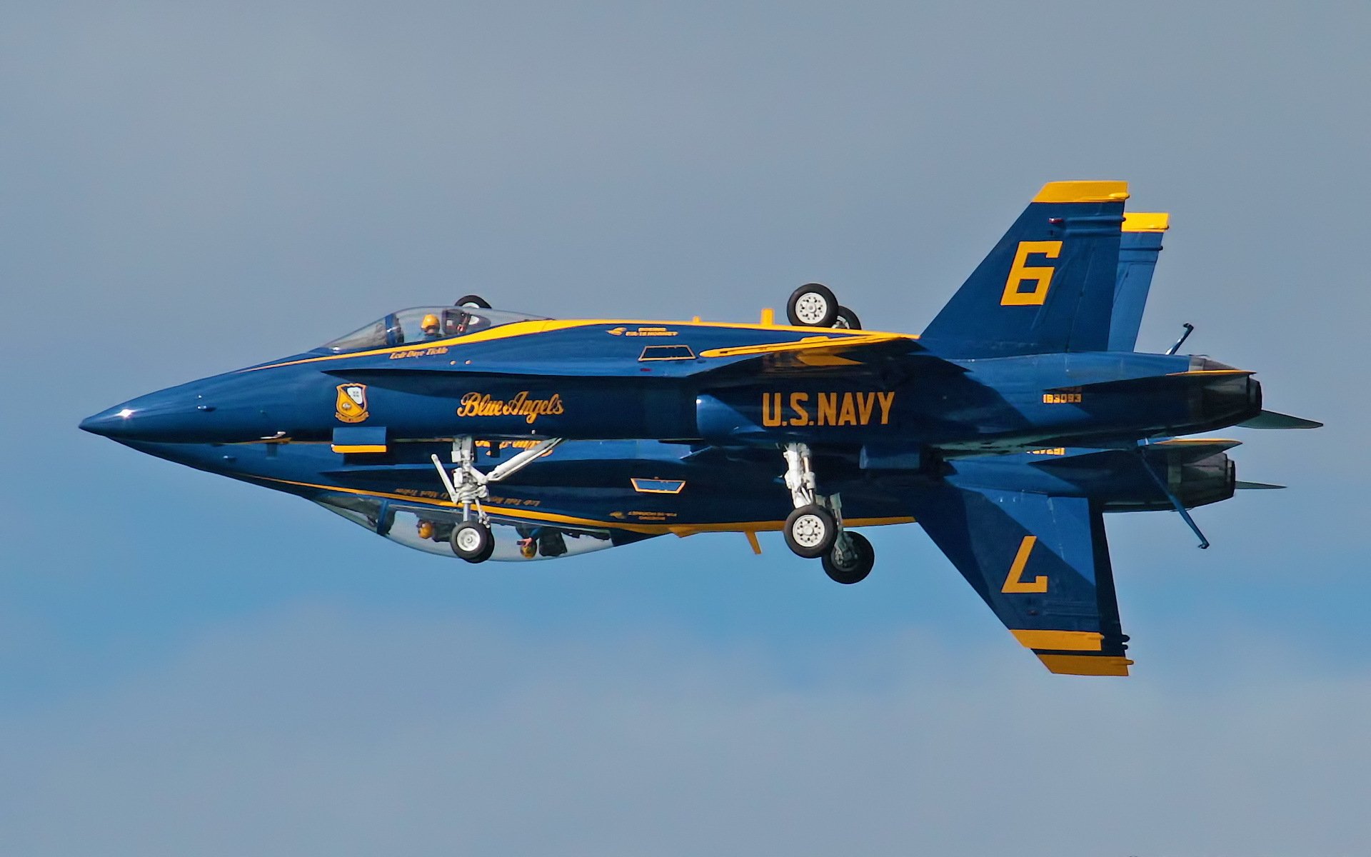 HD PC desktop wallpaper of a U.S. Navy Blue Angels aircraft vehicle (F/A-18) inverted with landing gear down, blue-and-gold livery against a pale sky.