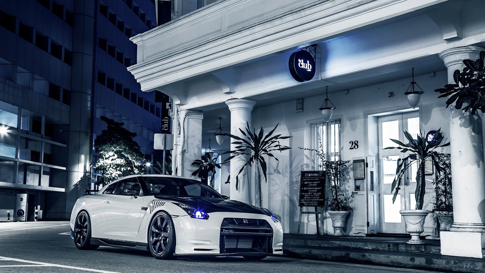 HD desktop wallpaper featuring a sleek white Nissan GT-R parked in front of a stylish urban building at night.