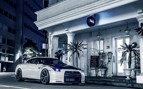 HD desktop wallpaper featuring a sleek white Nissan GT-R parked in front of a stylish urban building at night.