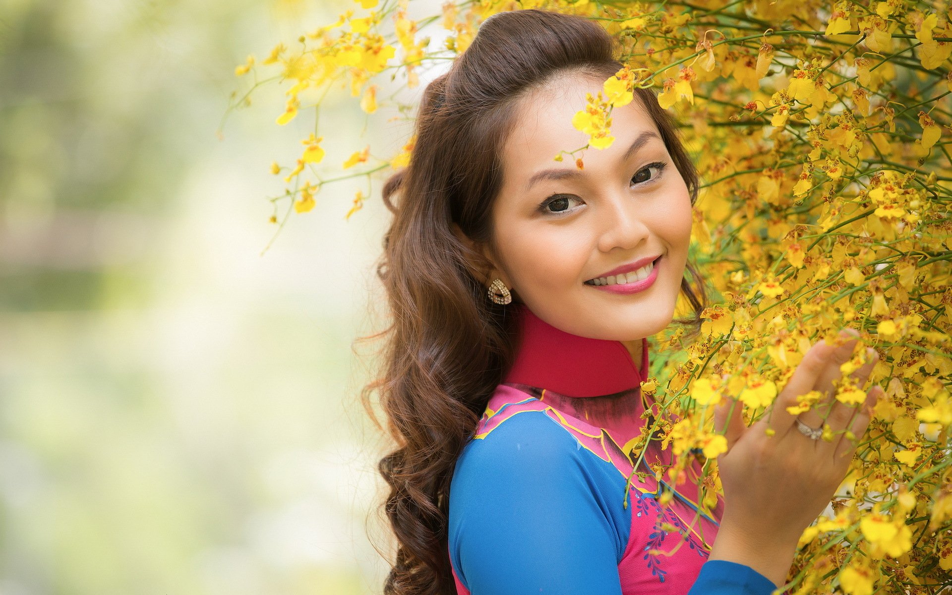 A smiling Asian woman in a colorful outfit poses among vibrant yellow flowers, creating a lively and cheerful HD PC desktop wallpaper and background.