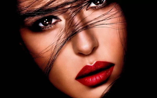 A stunning HD wallpaper featuring celebrity Monica Bellucci, capturing her captivating gaze and striking features with flowing hair and bold red lips against a dark background.