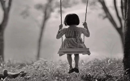 A little girl swings serenely in a natural setting, captured in a black-and-white photograph, making a charming HD desktop wallpaper and background.