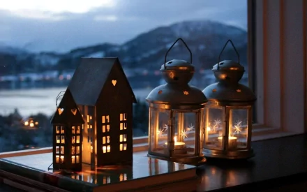 A serene HD desktop wallpaper featuring man-made lanterns and a small house-shaped light source glowing softly by a window with a snowy mountain view outside.