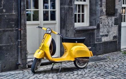 HD desktop wallpaper and background showing a vibrant yellow scooter parked on a cobblestone street against a rustic building facade.