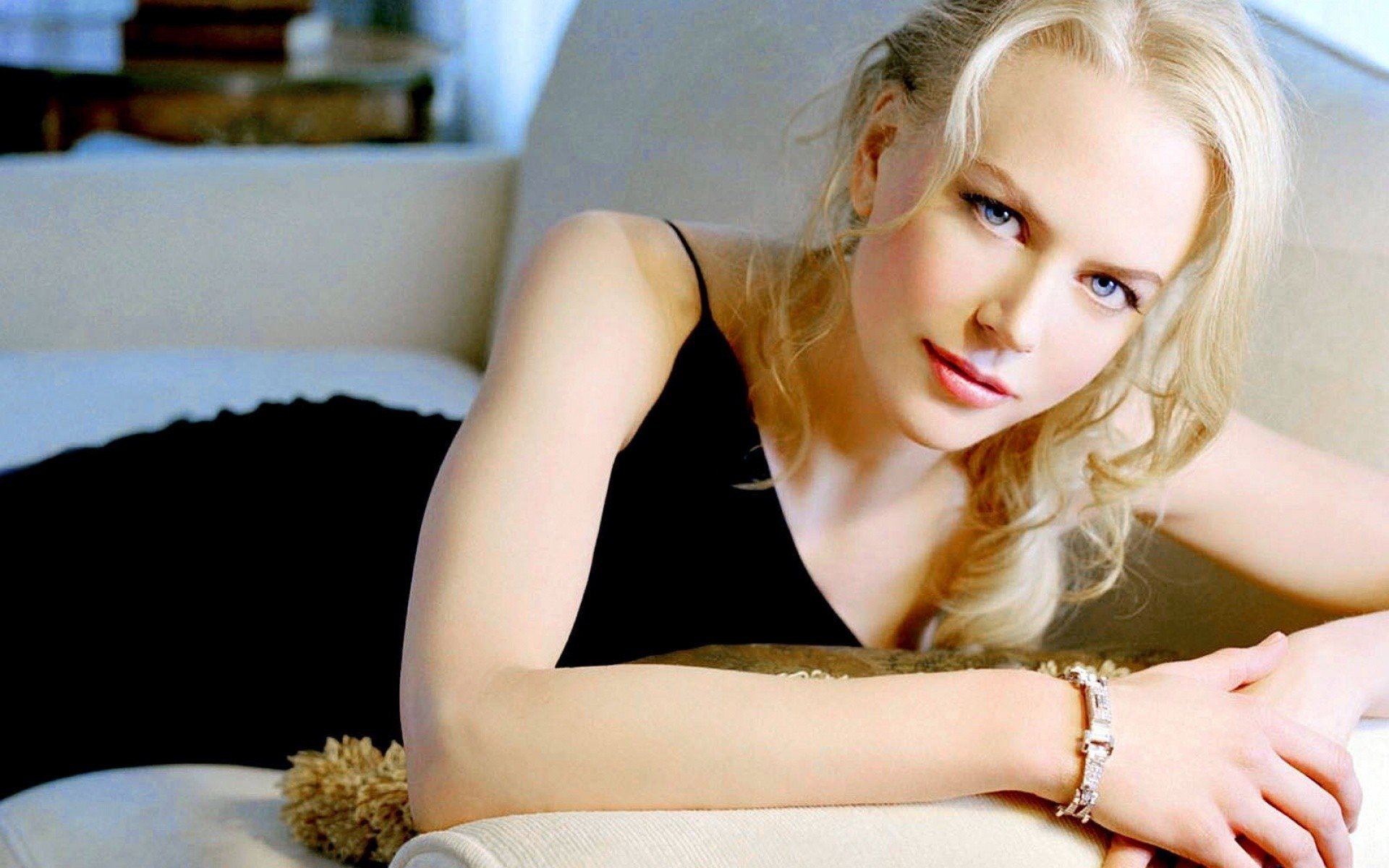 HD PC desktop wallpaper featuring a close-up of celebrity Nicole Kidman reclining on a light-colored couch, wearing a black outfit and subtle makeup.