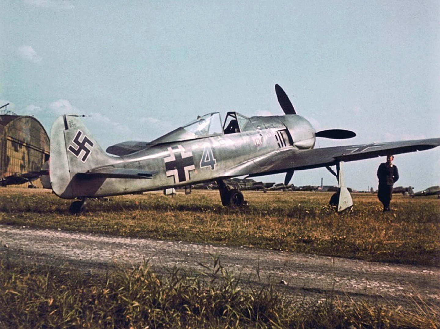 HD desktop wallpaper featuring a WWII-era Focke-Wulf Fw 190 military aircraft on the ground with a person nearby under a clear sky.