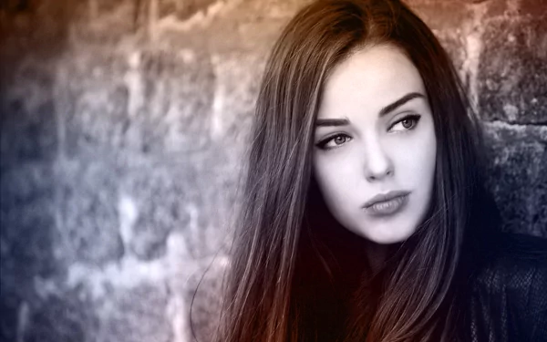 HD desktop wallpaper featuring a beautiful woman with long hair, looking off to the side against a textured stone wall background.