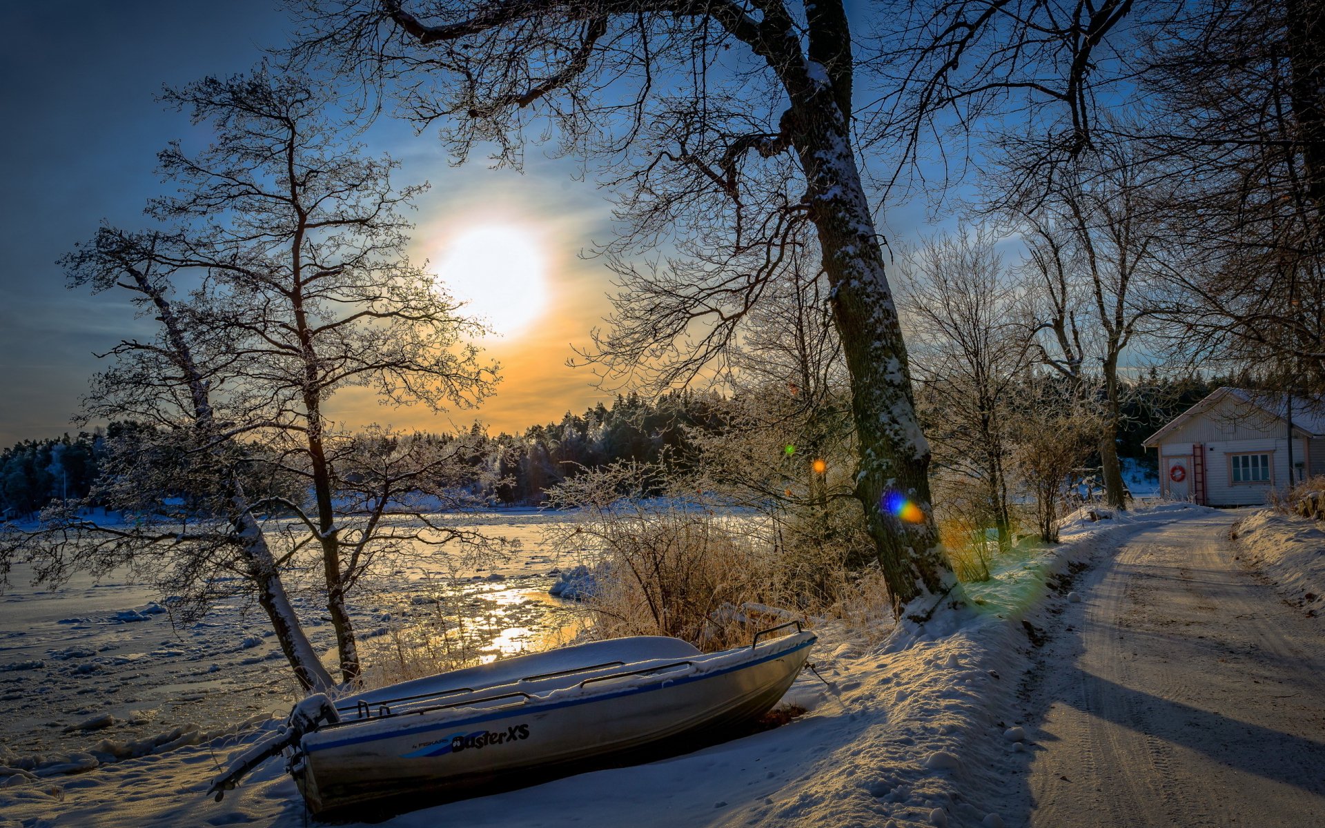 HD PC desktop wallpaper featuring a serene snowy landscape with a boat resting by the frozen shore under a bright sun and clear blue sky.