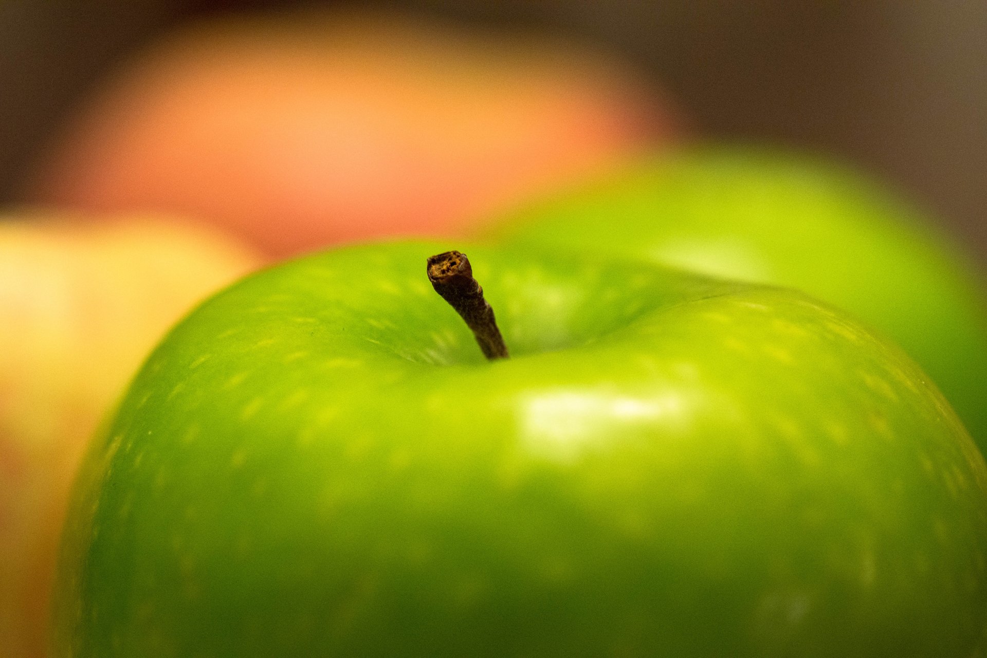 Close-up of a vibrant green apple with blurred apples in the background, featured as a crisp HD PC desktop wallpaper showcasing fresh fruit and food.