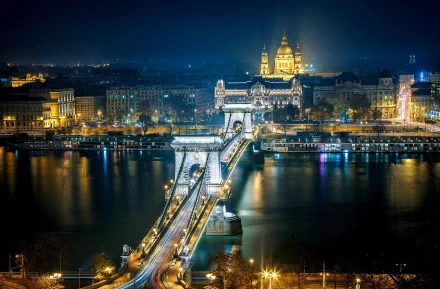 A stunning night view of Budapest's Chain Bridge, illuminated against the backdrop of the cityscape, featuring reflections on the river and the grandeur of nearby buildings.