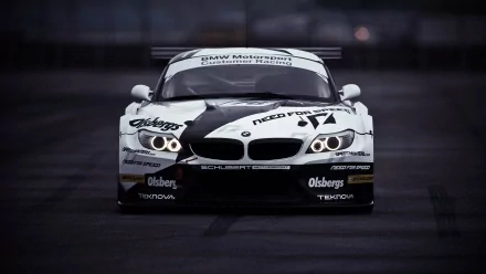 HD PC desktop wallpaper featuring a BMW race car with a black and white livery, captured head-on on a dark, blurred track background.