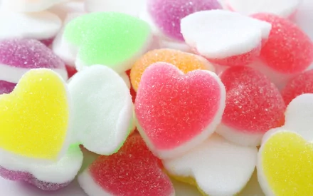 Colorful heart-shaped gummy candies scattered on a surface, creating a vibrant and sugary display. This image serves as an enticing HD desktop wallpaper and background.