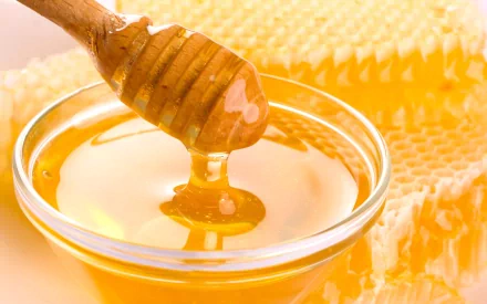A close-up of a wooden honey dipper drizzling golden honey into a glass bowl, with honeycomb pieces in the background. This vibrant image captures the essence of food and honey.