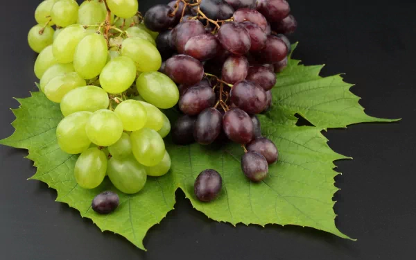A vibrant HD desktop wallpaper featuring fresh green and purple grapes arranged on a leaf, showcasing the beauty of nature and appetizing food.