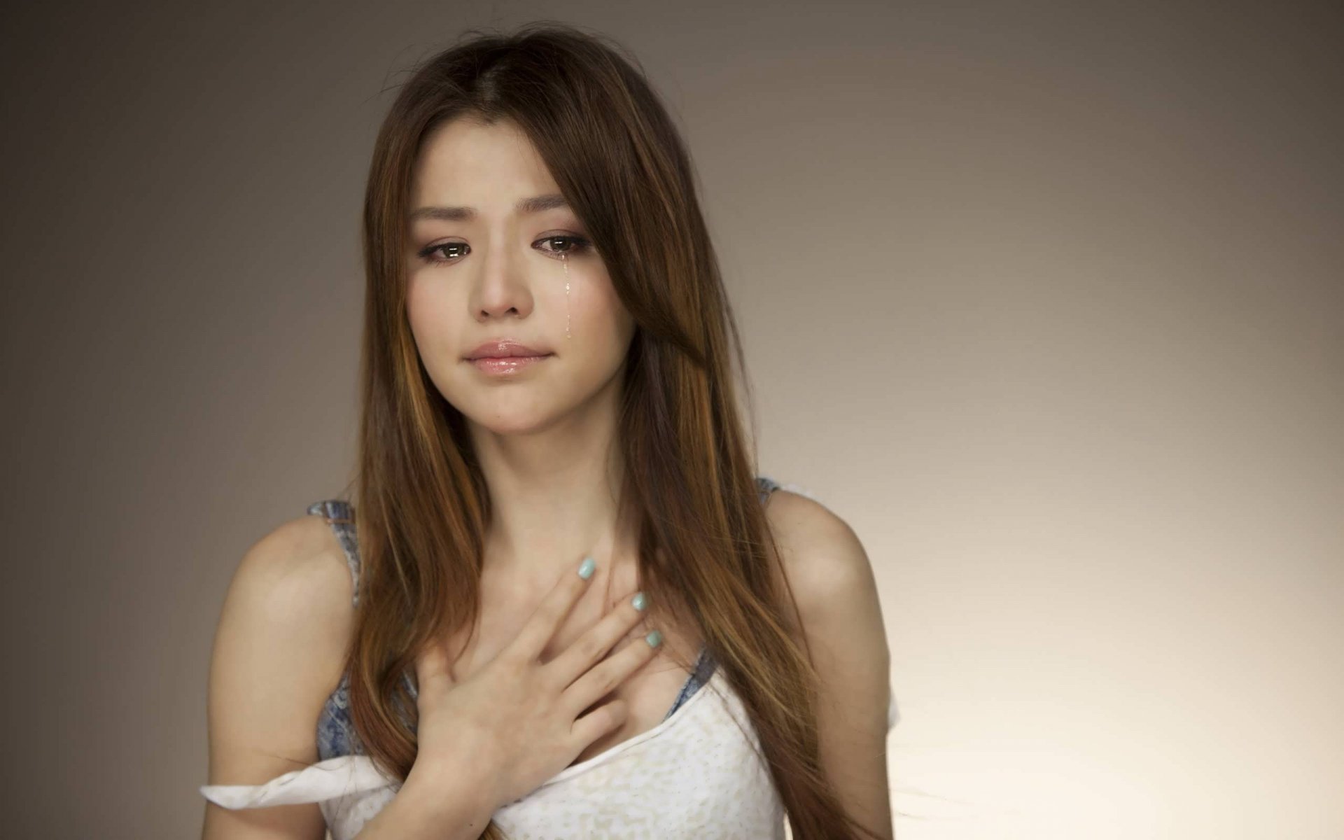 HD PC desktop wallpaper of a woman with long brown hair, softly lit against a neutral background, conveying a calm and introspective mood.