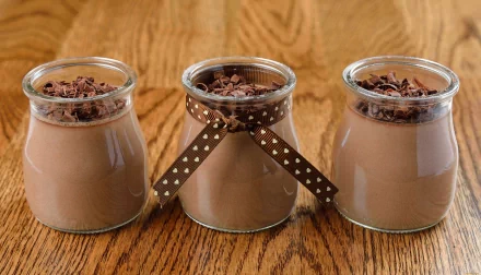 Three jars of creamy chocolate dessert topped with chocolate shavings, set against a warm wooden background. This 4K Ultra HD image captures a delightful food moment.