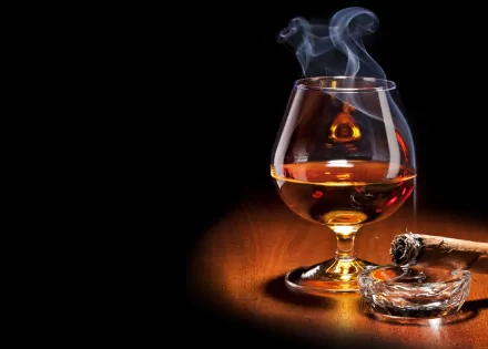 4K Ultra HD wallpaper showing a glass of brandy with rising smoke and a lit cigar resting on an ashtray against a dark background.