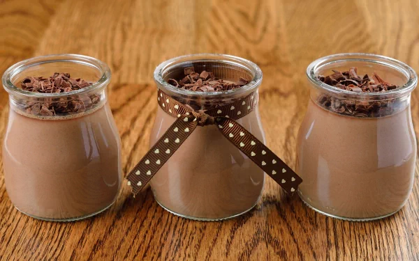 Three jars of creamy chocolate dessert topped with chocolate shavings, set against a warm wooden background. This 4K Ultra HD image captures a delightful food moment.