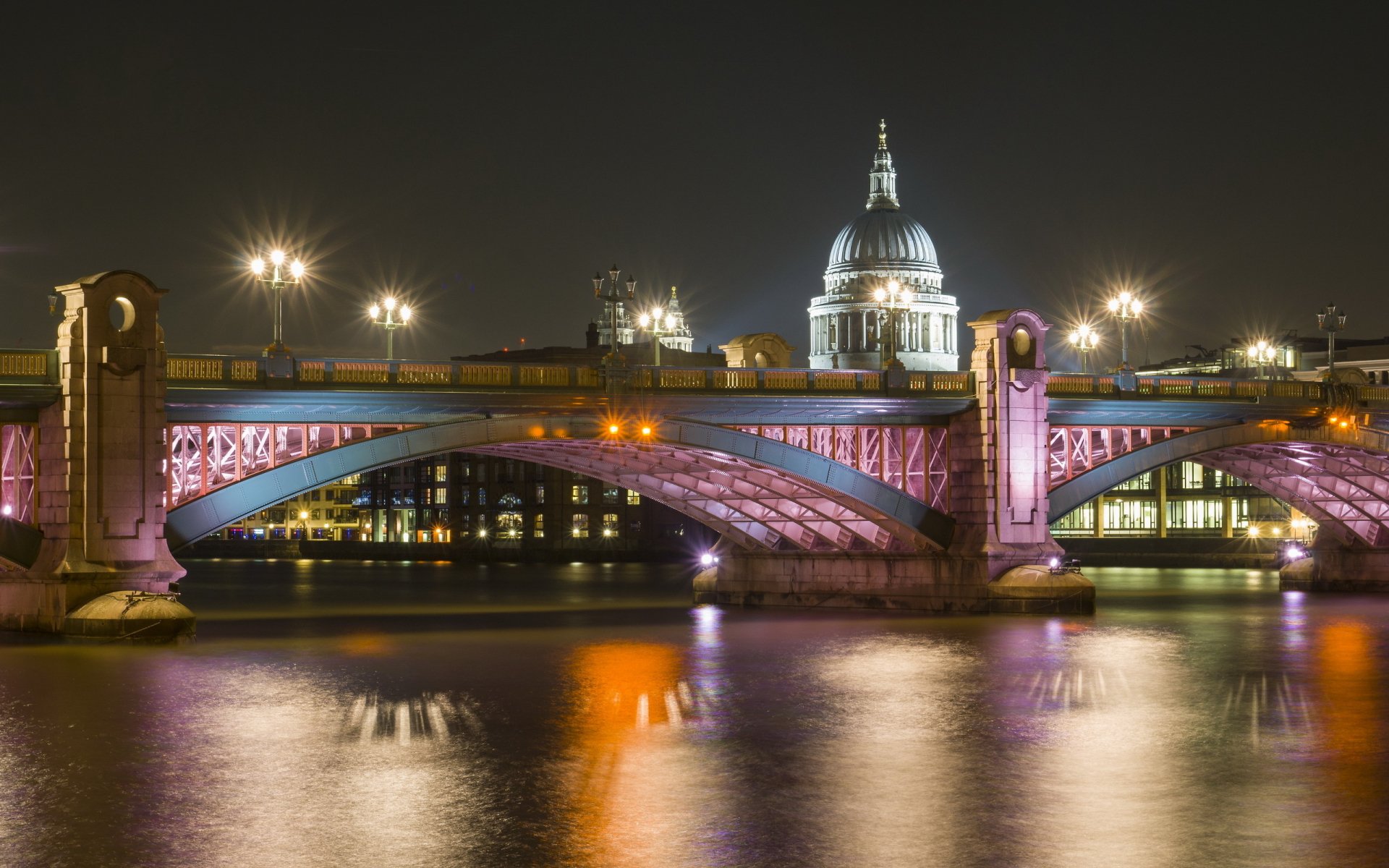 Night view of London's Southwark Bridge, man-made illuminated arches reflecting on the Thames with St. Paul's Cathedral in the background — 2K Quad HD PC desktop wallpaper.