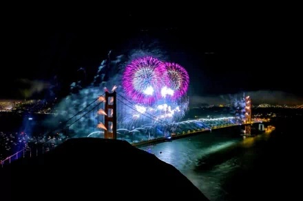 HD PC desktop wallpaper photography: vibrant fireworks burst over the Golden Gate Bridge at night, casting colorful reflections across the bay.