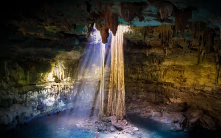 A stunning cave interior featuring sunlight streaming through a rock opening, illuminating a serene pool below, creating a captivating natural backdrop for desktop wallpaper.