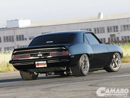 HD PC desktop wallpaper featuring a sleek black Chevrolet Camaro SS parked on a road with an industrial building in the background.