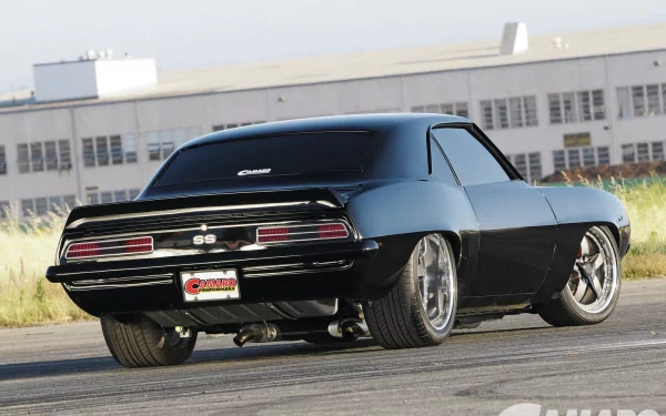 HD PC desktop wallpaper featuring a sleek black Chevrolet Camaro SS parked on a road with an industrial building in the background.