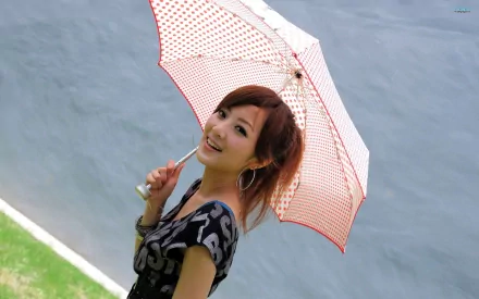 A woman, tagged as Mikako Zhang Kaijie, smiles while holding a red and white polka dot umbrella. She stands against a grayish background with a patch of green grass, in this HD desktop wallpaper.