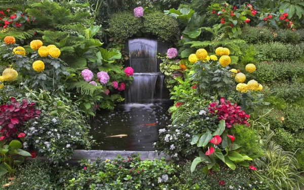 A lush man-made garden featuring a waterfall surrounded by vibrant flowers and greenery, captured in HD, serving as a serene desktop wallpaper and background.