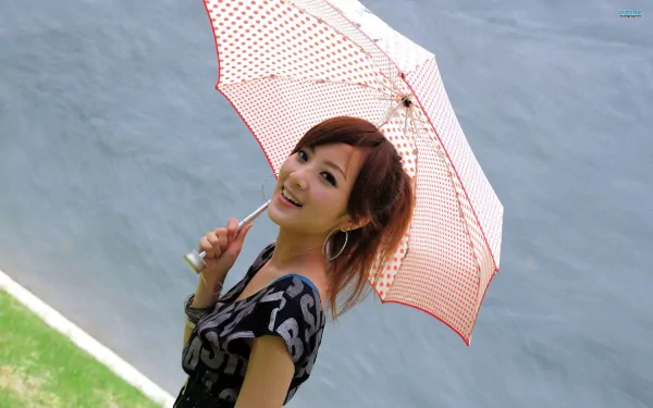 A woman, tagged as Mikako Zhang Kaijie, smiles while holding a red and white polka dot umbrella. She stands against a grayish background with a patch of green grass, in this HD desktop wallpaper.