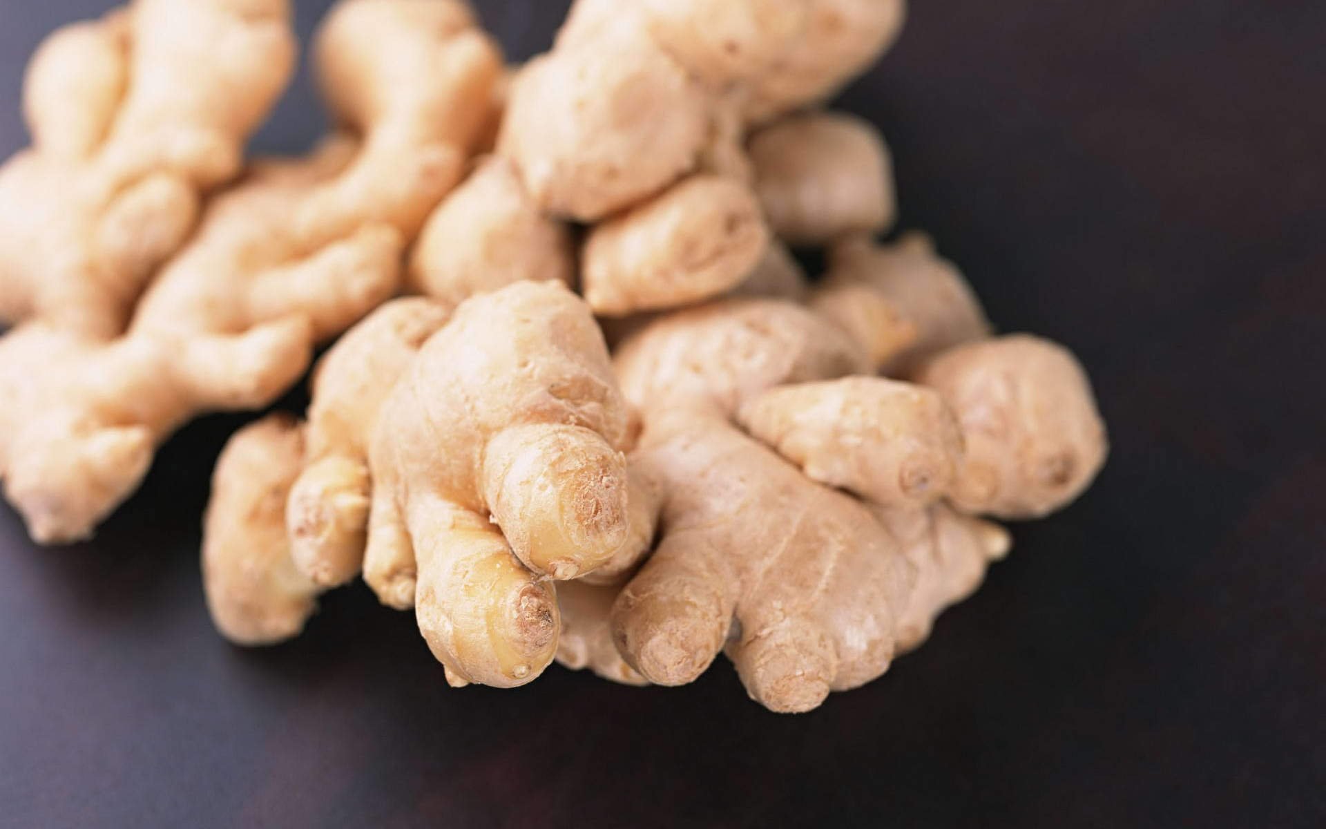 Close-up HD desktop wallpaper of fresh ginger roots with a dark background, highlighting the texture and natural color of the vegetable.