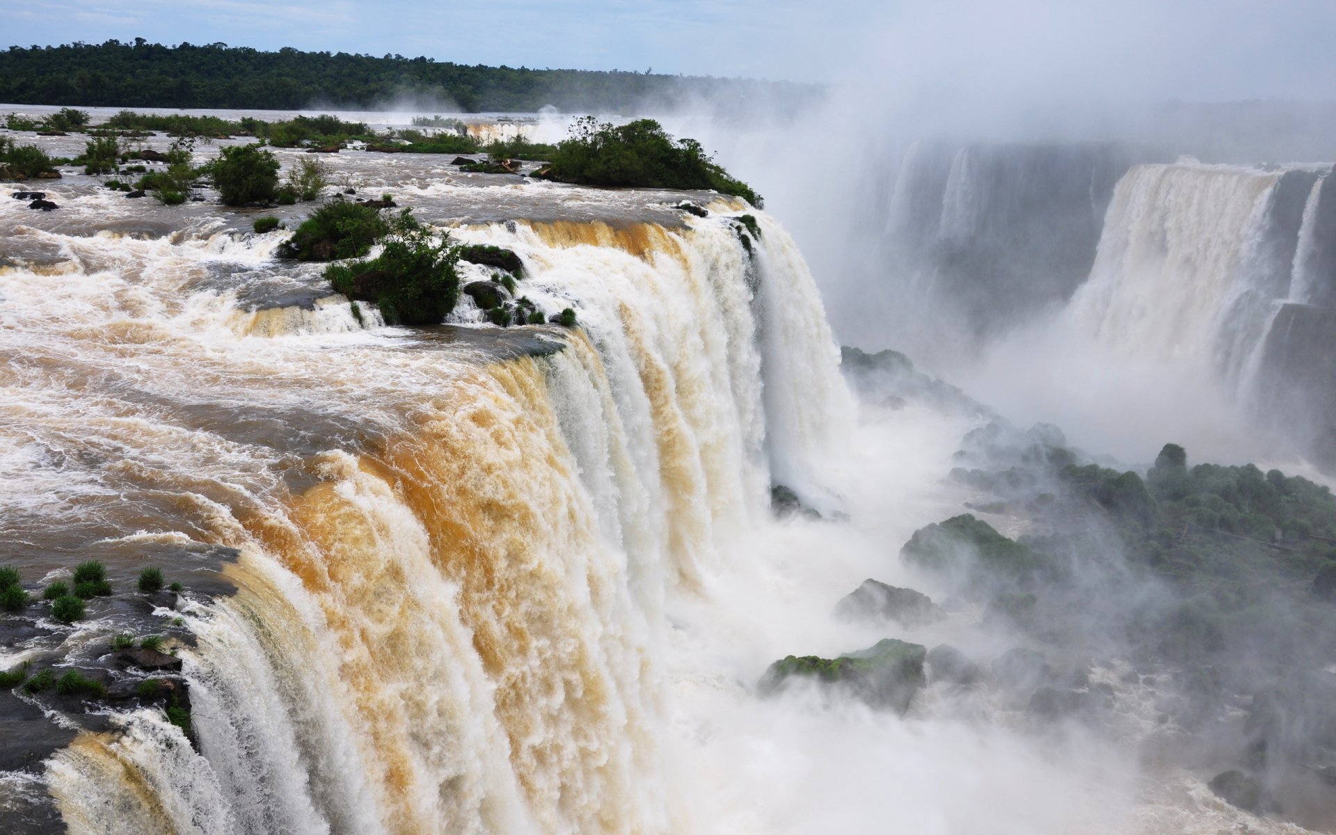 Iguazu Falls cascading powerfully over lush cliffs, surrounded by mist and greenery, captured in a vibrant HD nature scene for a PC desktop wallpaper.