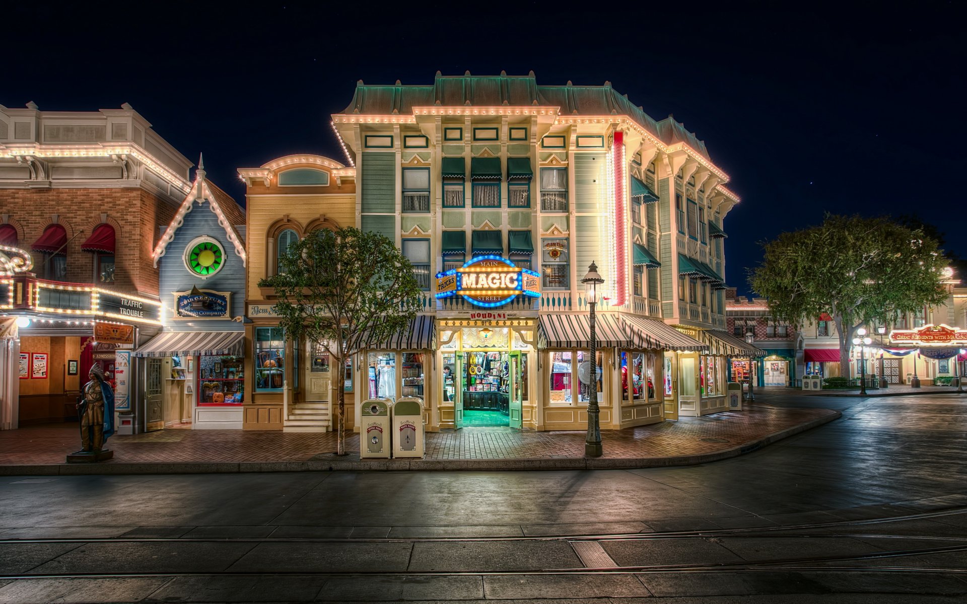HD desktop wallpaper of a brightly lit, man-made town street scene at night, showcasing charming buildings and storefronts with illuminated signs and trees.