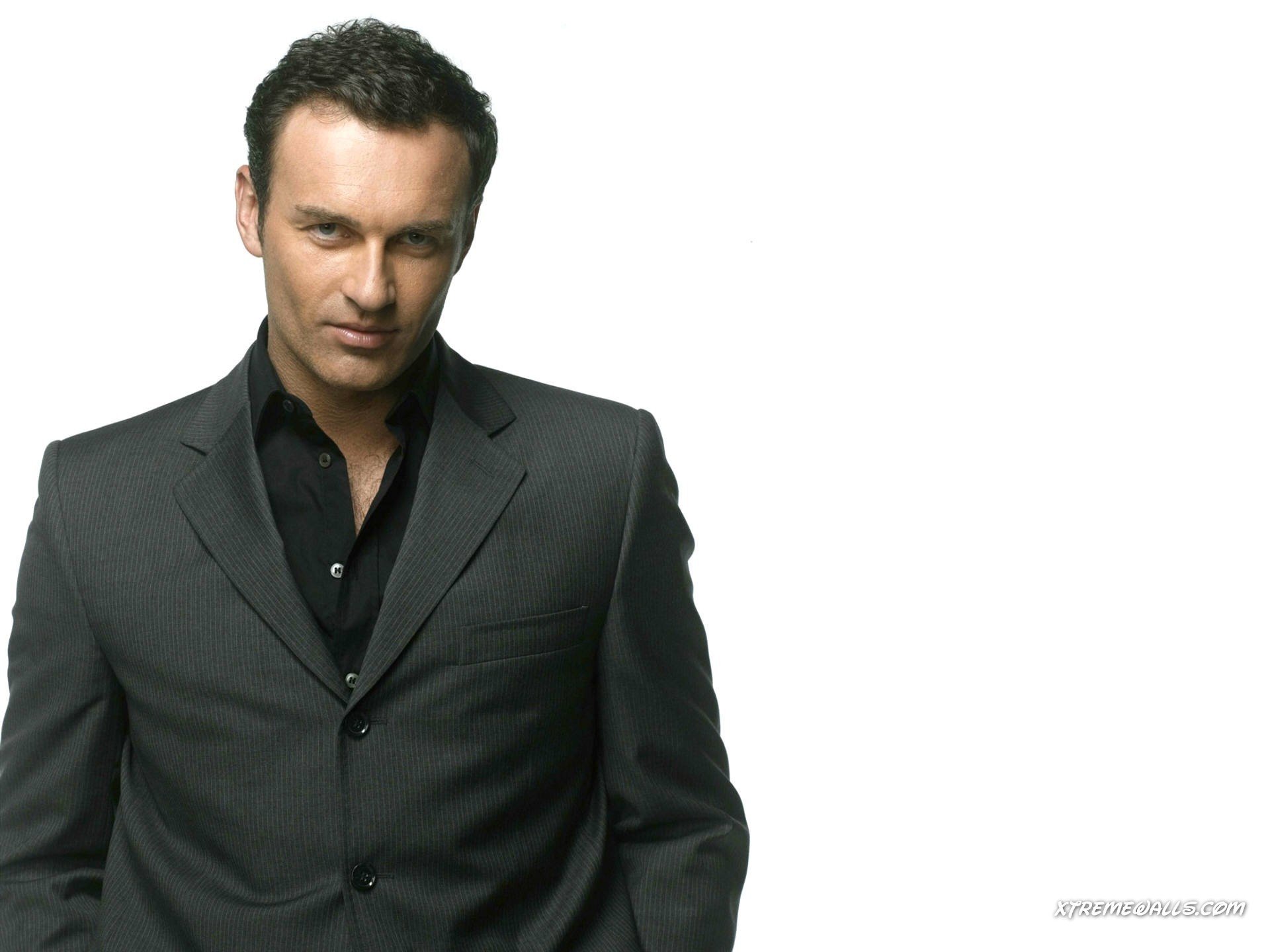 HD PC desktop wallpaper of a male celebrity in a tailored dark suit, posing confidently against a clean white background.