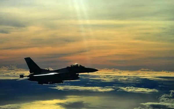 A military jet fighter soars through a vibrant sky, showcasing sleek design against a backdrop of clouds and a colorful sunset. Perfect HD wallpaper for aviation enthusiasts.