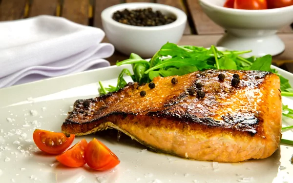 A vibrant plate of grilled fish garnished with salad, peppercorns, and cherry tomatoes, set against a rustic wooden background. A striking 4K Ultra HD desktop wallpaper.