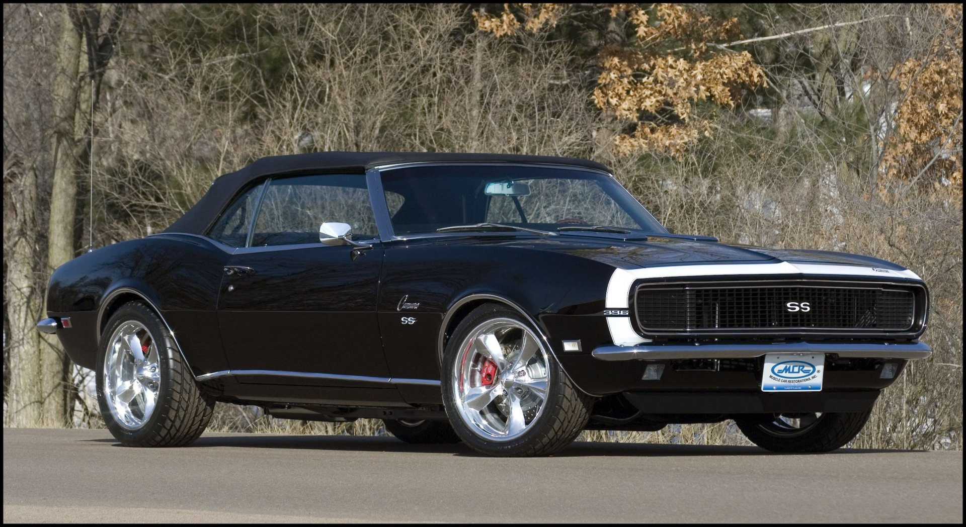 HD PC desktop wallpaper featuring a sleek black Chevrolet Camaro SS convertible parked on a road with autumn trees in the background.