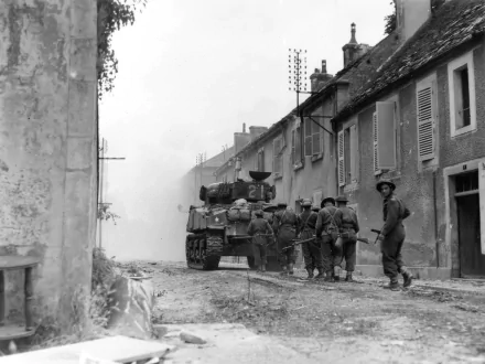 Black and white World War II military scene with soldiers and a tank moving through a narrow village street, captured in an HD PC desktop wallpaper background.