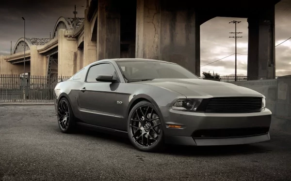 HD PC desktop wallpaper featuring a sleek gray Ford Mustang parked under an urban bridge with dramatic lighting and a moody sky.