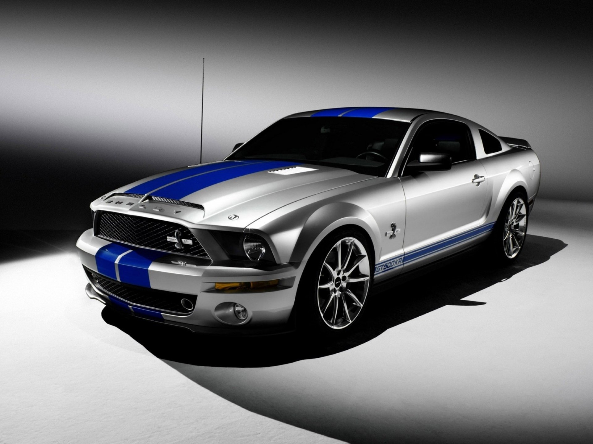 A sleek silver Ford Mustang with blue racing stripes, showcased in an HD PC desktop wallpaper, exuding power and style against a striking backdrop.