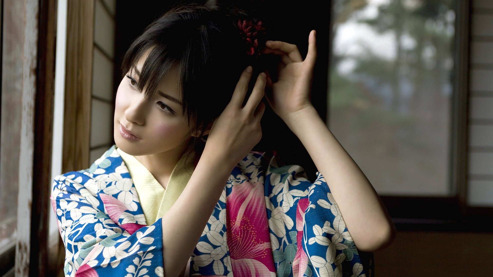 HD desktop wallpaper featuring an Asian woman in a blue and pink floral kimono, standing by a window, gracefully adjusting her hair.
