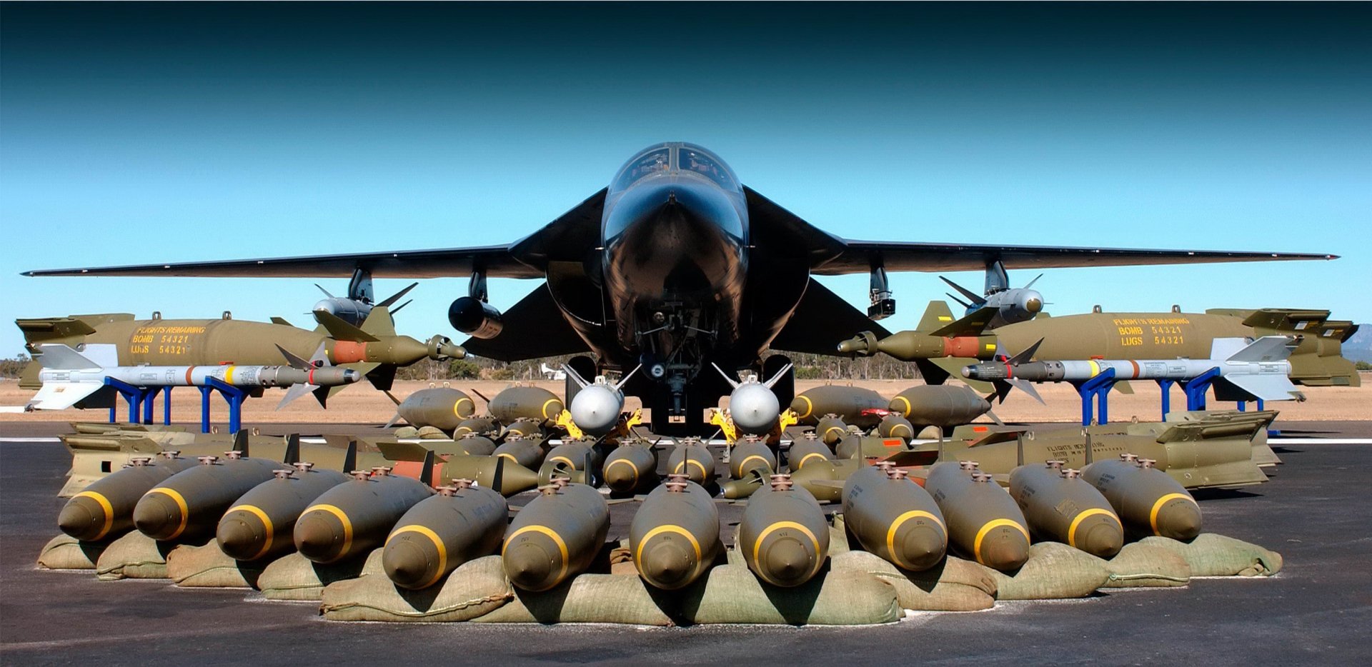 HD desktop wallpaper featuring a military General Dynamics F-111 Aardvark jet with an array of bombs displayed in the foreground on a runway.
