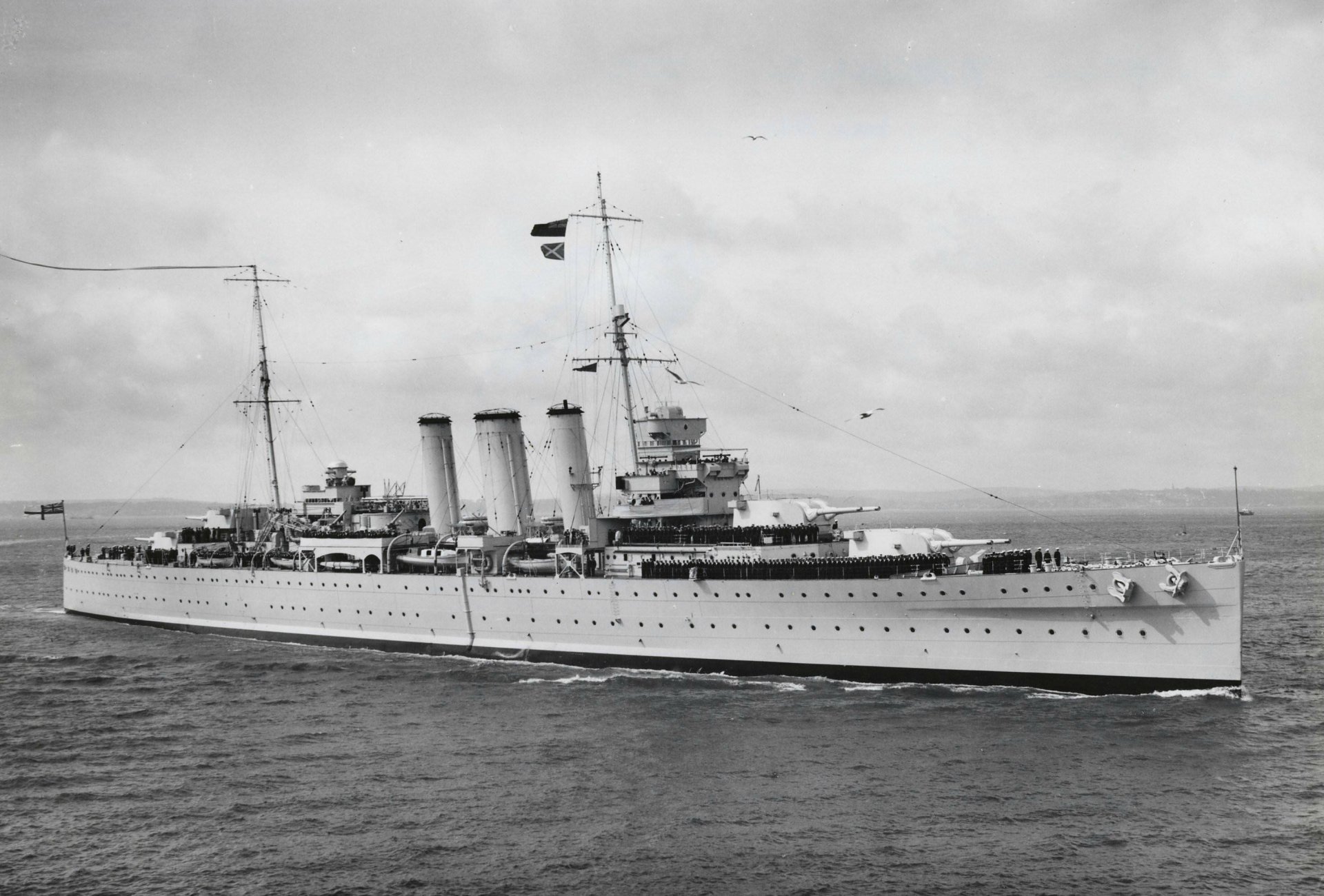 Black and white image of the Royal Navy cruiser HMS Cornwall (56) sailing on calm waters, captured as an HD desktop wallpaper background.