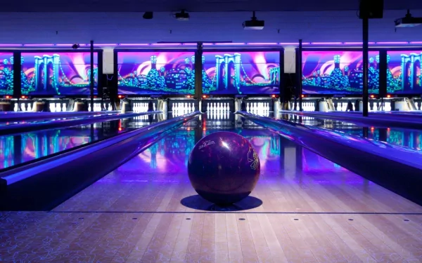 A vibrant bowling alley featuring a purple bowling ball on the lane, surrounded by glowing screens and colorful lights, captures the excitement of sports in this HD desktop wallpaper.